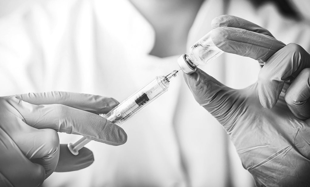 Doctor drawing vaccine from a vial using a syringe